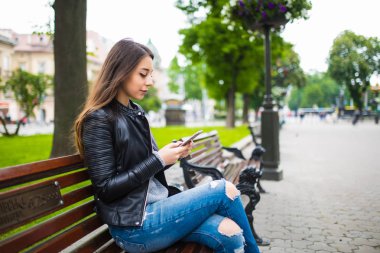 Açık bankta oturan ve telefonda yazarak güzel genç kadın