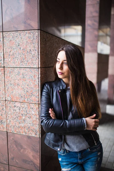Красивая молодая девушка в стильной куртке возле зданий на улице — стоковое фото