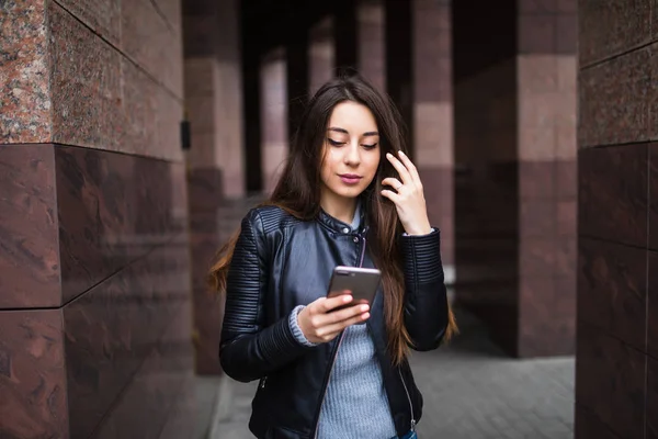 Ofis binaları içinde belgili tanımlık geçmiş ile bir akıllı telefon kullanan genç kadın