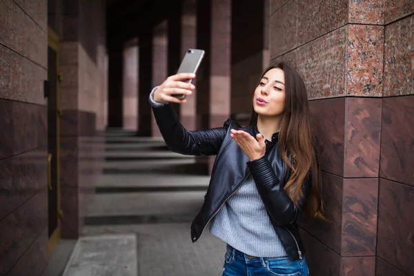 Csinos, fiatal nő, amelyek séta, és így selfie épület utca közelében — Stock Fotó