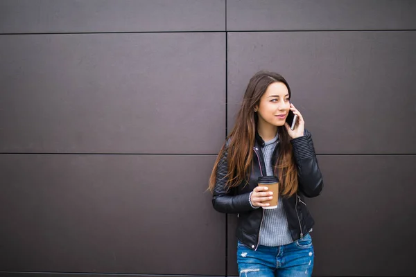 Mujer sonriente hablando por teléfono con taza de café sobre el fondo de la pared — Foto de Stock