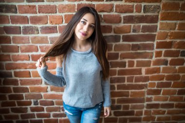 Rahat kıyafet eller oynamak gülümseyerek, beyaz duvara karşı ayakta saçlı güzel genç kadın