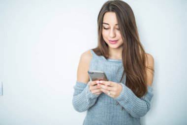 Manifatura arkadaş için. Akıllı telefon tutarak ve gri arka plan karşı dururken gülümsemeyle bakarak çekici genç kadın