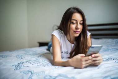 Mutlu kadın smartphone cep telefonu ile kısa mesaj okuma yatakta oturuyordu. Gülümseyen kız yatak odasında bir oda arkadaşı ile görüşmesinde rahat oturuyor. Gülümseyen kadın evde cep telefonu ile net sörf.