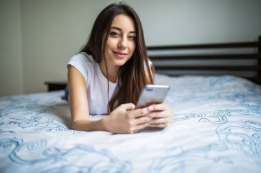 Mutlu kadın smartphone cep telefonu ile kısa mesaj okuma yatakta oturuyordu. Gülümseyen kız yatak odasında bir oda arkadaşı ile görüşmesinde rahat oturuyor. Gülümseyen kadın evde cep telefonu ile net sörf.