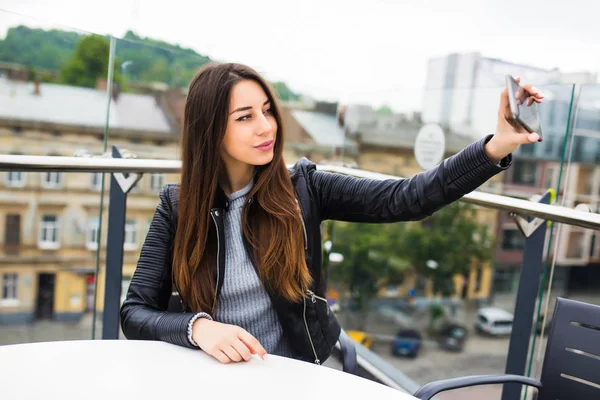 Mujer feliz haciendo retrato selfie de pie en la terraza con rascacielos en el fondo — Foto de Stock