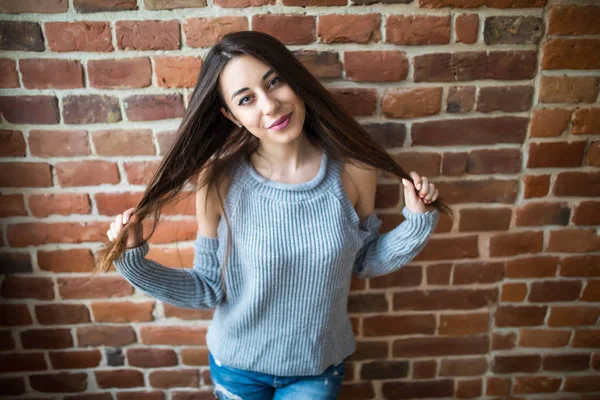 Mooie jonge vrouw in vrijetijdskleding lacht, permanent tegen witte bakstenen muur — Stockfoto