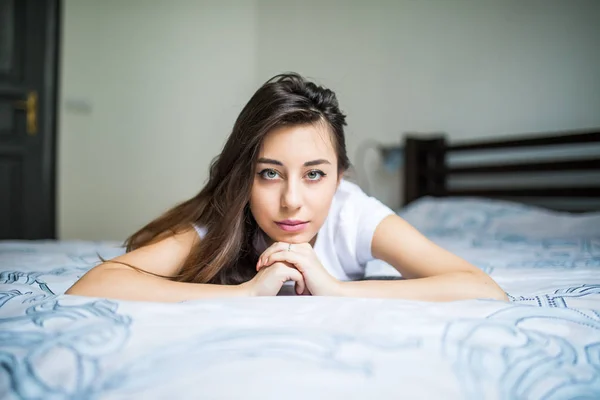 Genç kadın, gülümseyerek başını eliyle saçlarını diğerinde üzerine istirahat yatağın ucundaki yalan. — Stok fotoğraf