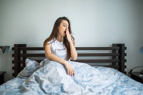 Jovem mulher sentada na cama e bocejando em casa — Fotografia de Stock