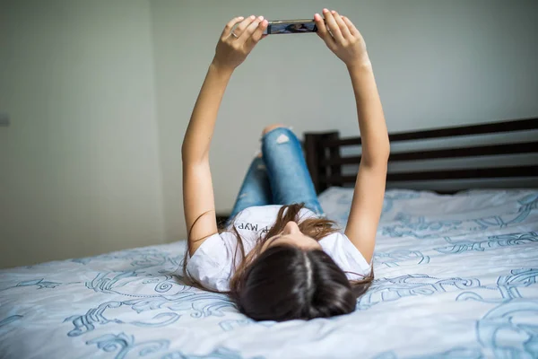 Happy woman lying on the bed and making selfie photo on smartphone at home — Stock Photo, Image