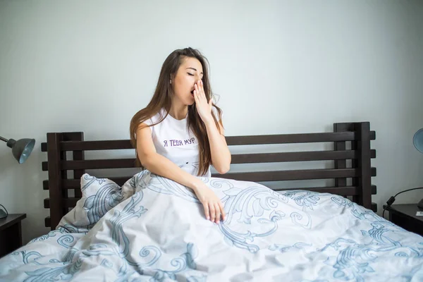 Jovem mulher sentada na cama e bocejando em casa — Fotografia de Stock