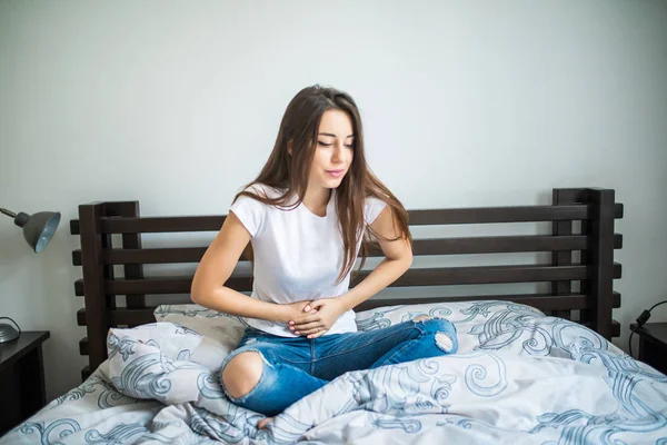 Jeune femme beauté souffrant de douleurs abdominales tout en étant assis sur le lit à la maison — Photo