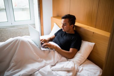 Bir dizüstü bilgisayarda evde çalışma yatakta yatan genç adam