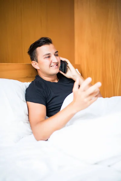 Мужчина, использующий свой мобильный телефон в своей спальне утром — стоковое фото