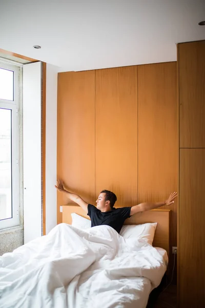 Портрет молодого человека, протягивающего руки в постели дома утром — стоковое фото