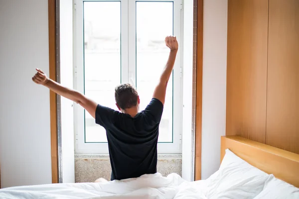 Вид сзади на молодого человека, просыпающегося в постели и вытягивающего руки утром — стоковое фото