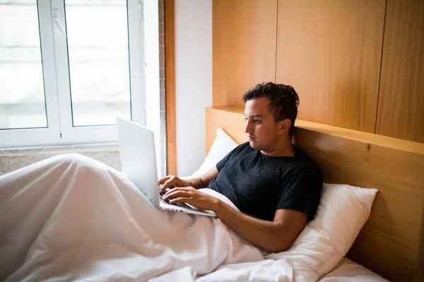 Joven acostado en la cama trabajando en un portátil en casa — Foto de Stock