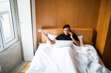 Laptop ve konuşma telefon cevap ile çalışma sabah yatakta yatan yakışıklı adam