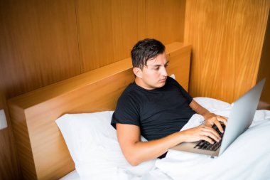 Bir dizüstü bilgisayarda evde çalışma yatakta yatan genç adam