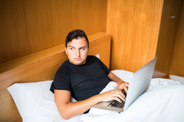 Joven acostado en la cama trabajando en un portátil en casa — Foto de Stock