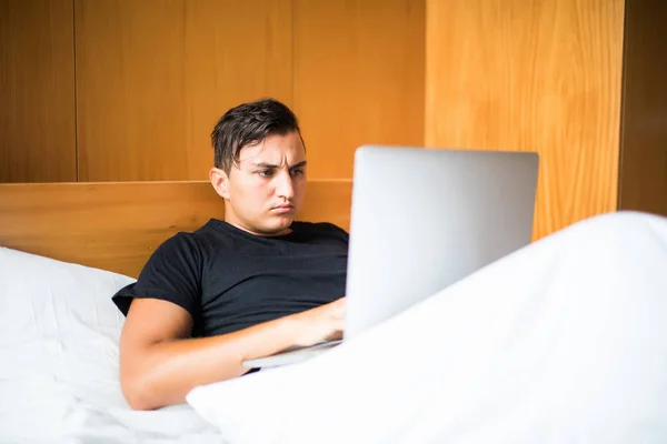 Joven acostado en la cama trabajando en un portátil en casa — Foto de Stock
