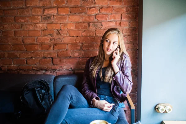 Vidám fiatal nő beszél telefonon, és mosolyogva, miközben élvezi a kávét a café — Stock Fotó