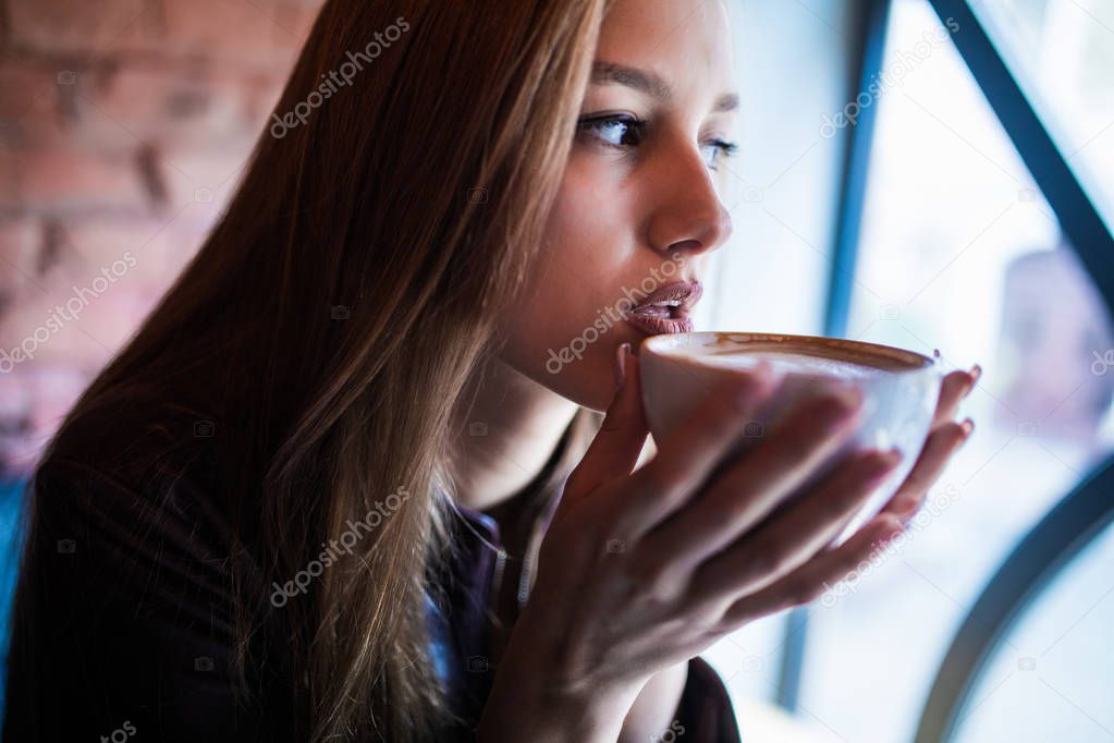 Close-up portrait of a pretty woman smiling and drinking coffee in cafe.