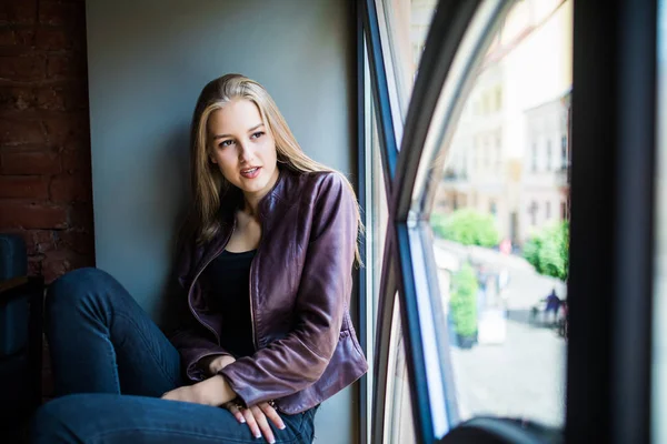 Νεαρή γυναίκα κάθεται σε ένα περβάζι του παραθύρου σε ένα καφενείο και να απολαύσετε τον ελεύθερο χρόνο — Φωτογραφία Αρχείου