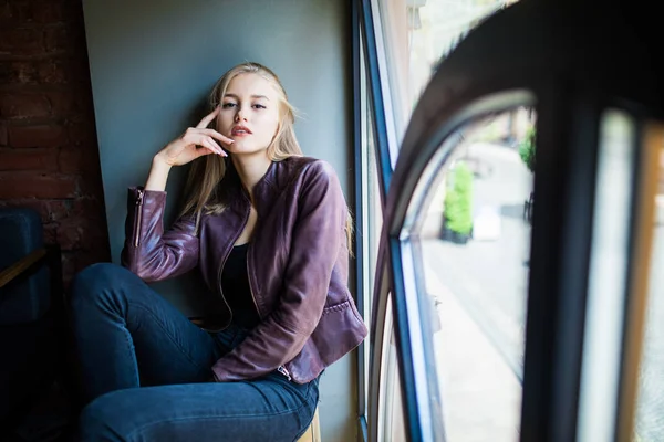 Fiatal nő ül egy ablakpárkányon egy kávézóban, és élvezze a szabad idő — Stock Fotó