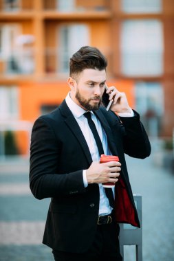Şehirde cep telefonu kullanan ve kahve içen kendine güvenen genç bir işadamı.