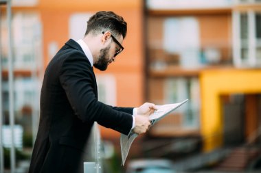 Yakışıklı sakallı işadamı Klasik takım elbiseli bir gazete okuyor ve balkonda dururken gülümseyen