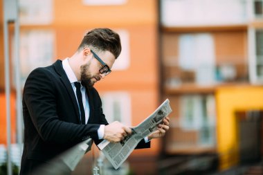 Yakışıklı sakallı işadamı Klasik takım elbiseli bir gazete okuyor ve balkonda dururken gülümseyen