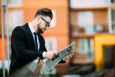 Yakışıklı sakallı işadamı Klasik takım elbiseli bir gazete okuyor ve balkonda dururken gülümseyen