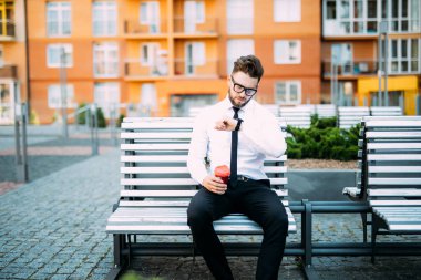 Genç işadamı kahve içme ve zamanında saat sokak bak işten dinlenme. Kahve molası için işadamı