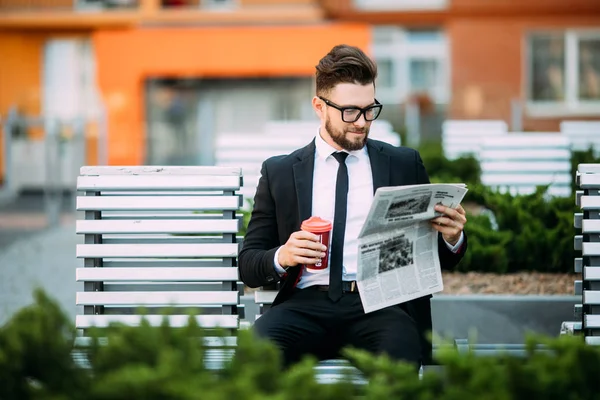 Продуманий бізнесмен з газетами і чашкою кави сидить на лавці — стокове фото