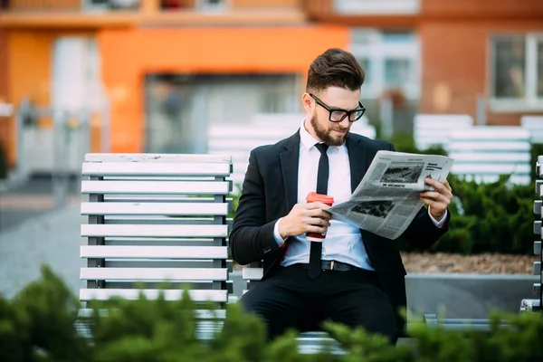 Tankeväckande affärsman med tidning och kaffe kopp sitter på bänk — Stockfoto