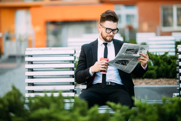 Pohledný podnikatel čtení finanční noviny zatímco sedí na lavičce venku — Stock fotografie