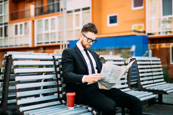 Bankta oturan gazete ve kahve Kupası ile düşünceli işadamı