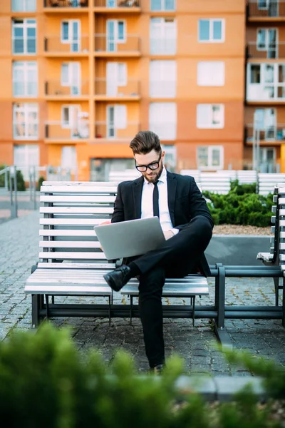 Giovane uomo d'affari seduto alla panchina a lavorare su laptop e bere caffè del mattino — Foto Stock