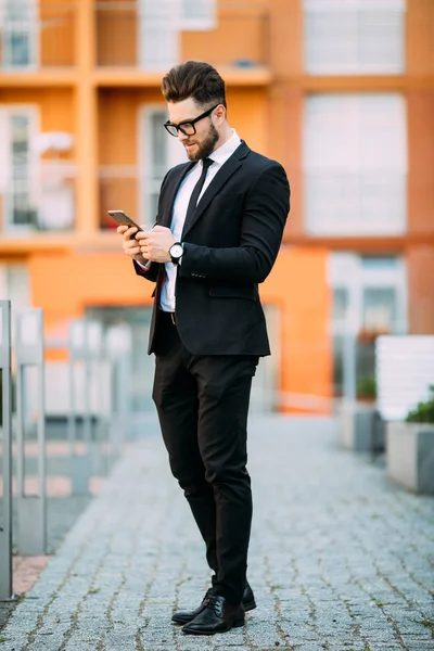 Hezký vousatý podnikatel v klasickém obleku používá chytrý telefon, když stál na balkóně úřadu — Stock fotografie