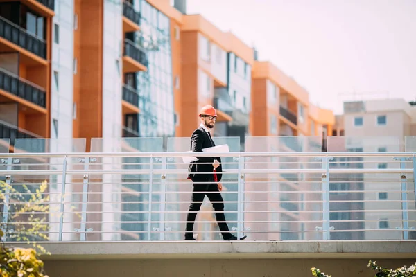 Handome adam sitesi yüklenici mühendis kask mavi holding ile inşaat alanında kağıt yürüyüş yazdırmak, arka plan vinç.