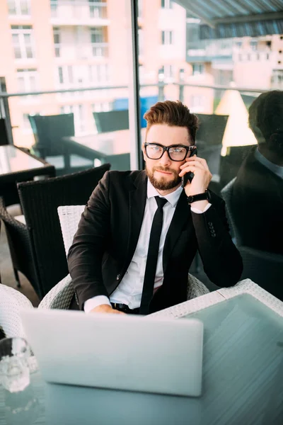 takım elbise dışında bir teras bir yerde bir kahve dükkanında konuşmak telefon laptop ile rahatlatıcı yakışıklı iş adamı