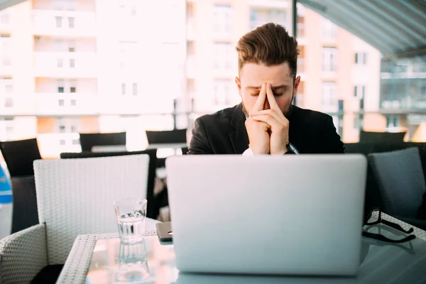 Красивий бізнесмен прокидається біля ноутбука з головним болем у кафе на терасі . — стокове фото
