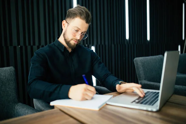 Sonriente hombre de negocios con computadora portátil y escribir aviso en documentos en la oficina — Foto de Stock