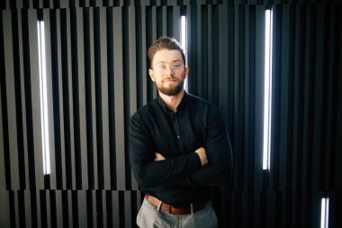 İyimser bir yakışıklı genç işadamı duran karşı modern ofis duvar iken seyir silah geçiş ile kameraya portresi