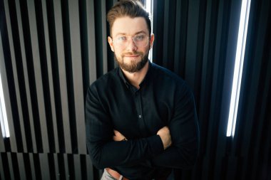 İyimser bir yakışıklı genç işadamı duran karşı modern ofis duvar iken seyir silah geçiş ile kameraya portresi