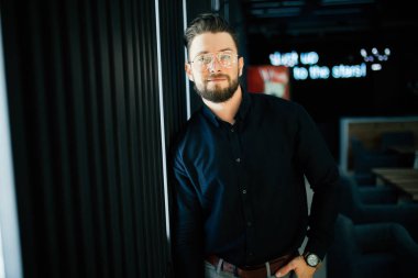 İyimser bir yakışıklı genç işadamı duran karşı modern ofis duvar iken seyir silah geçiş ile kameraya portresi