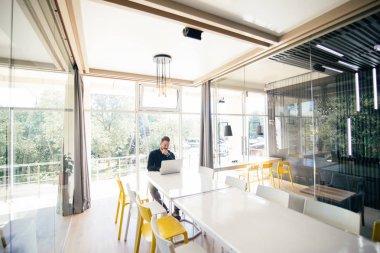 Büyük konferans romm beyaz masada oturan ve dizüstü toplantıdan önce çalışan sakallı yakışıklı işadamı