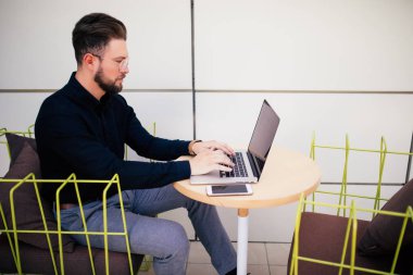 Yakışıklı genç sakallı işadamı kent merkezindeki kafede otururken bir laptop kullanıyor