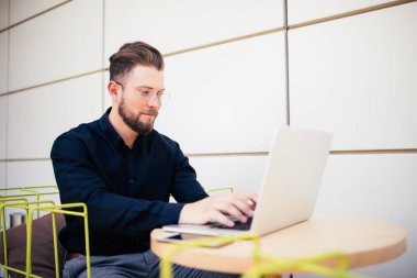 Yakışıklı genç sakallı işadamı kent merkezindeki kafede otururken bir laptop kullanıyor
